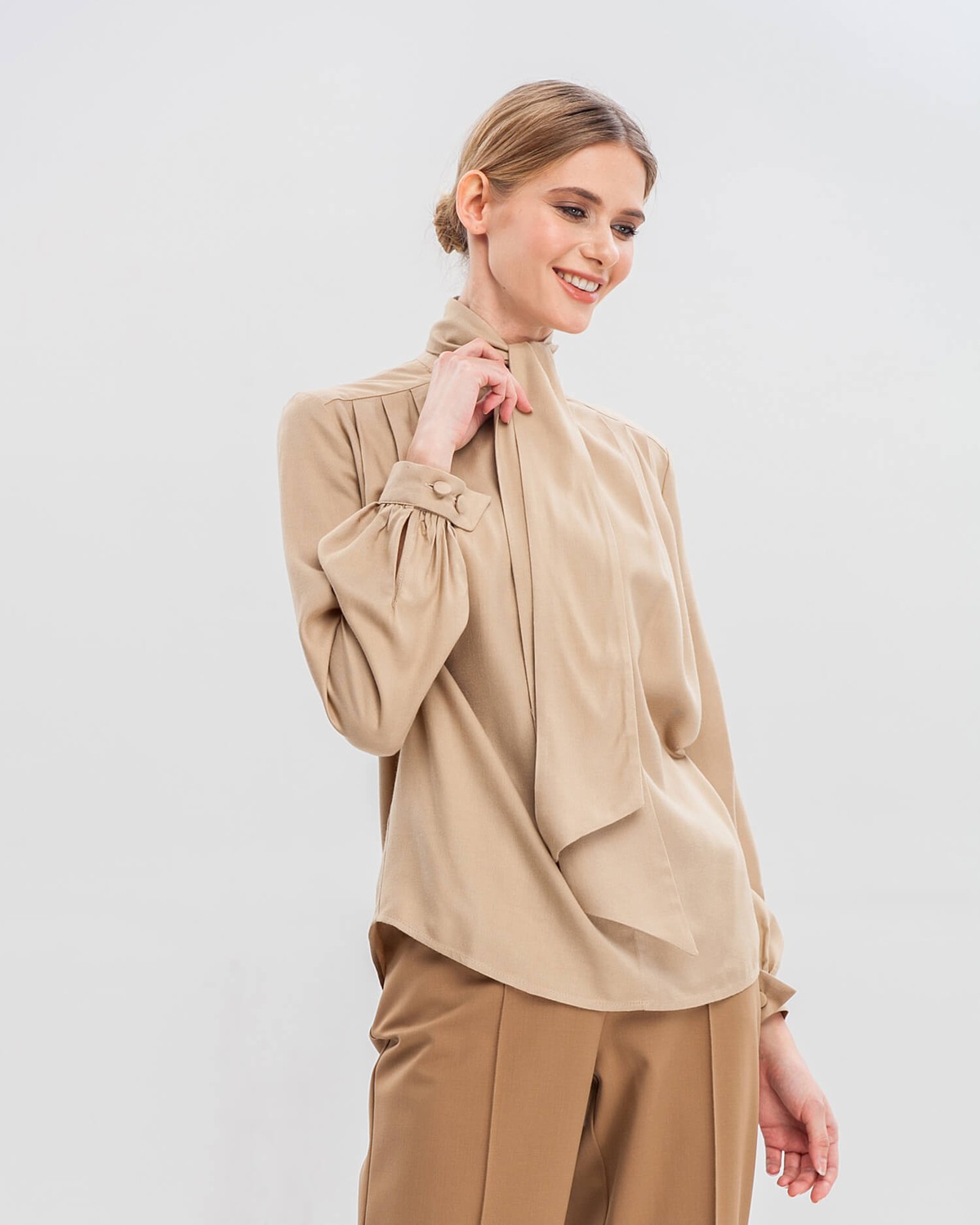 Блуза с широкими рукавами, узкими манжетами, драпировкой и бантом на груди добавит женственности любому деловому образу.
