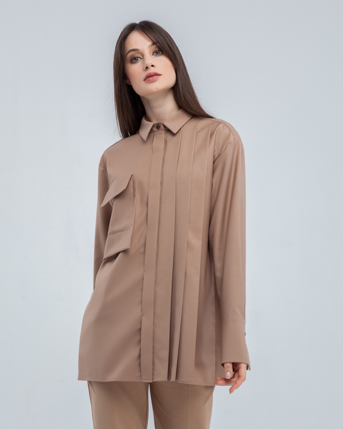 Акцентная удлиненная рубашка с объемным накладным карманом и плиссировкой по левому боку. Дополнена поясом на пуговицах в тон изделия. Модель позволяет носить ее как с поясом, так и без. Идеальный вариант для создания уникального делового или повседневного образа.

На модели размер XS