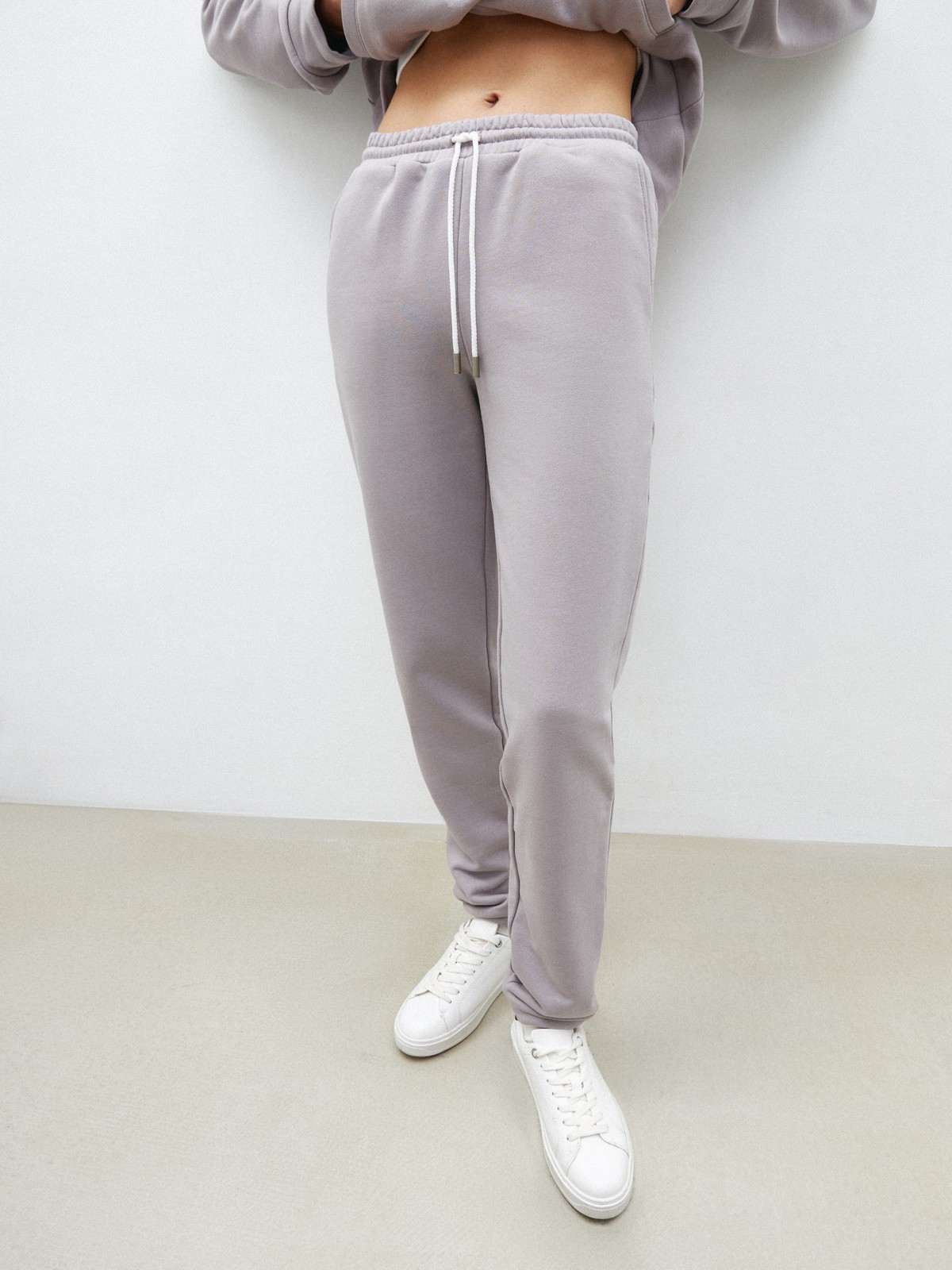 Брюки свободного спортивного силуэта. Модель дополнена манжетами из основной ткани по низу изделия и карманами по боковым швам. На поясе у брюк пояс, регулируемый завязками. Дополните свой образ толстовкой в тон изделия.

На модели размер XS