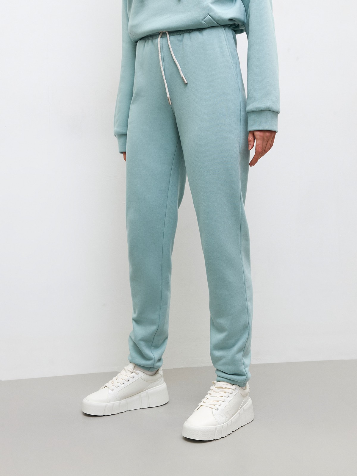 Брюки свободного спортивного силуэта. Модель дополнена манжетами из основной ткани по низу изделия и карманами по боковым швам. На поясе у брюк пояс, регулируемый завязками. Дополните свой образ толстовкой в тон изделия.

На модели размер XS