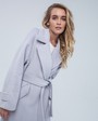 Пальто-халат длины миди с клапанами на карманах, рукавом реглан. Дополнено декоративными отстрочками и воротником-стойка с фигурным вырезом. Данная модель красиво подчеркивает женственные формы за счет пояса.

На модели размер XS