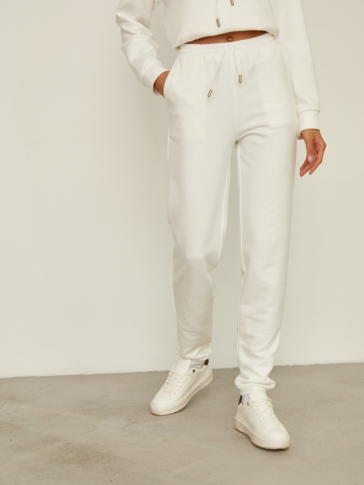 Брюки свободного спортивного силуэта. Модель дополнена манжетами из основной ткани по низу изделия и карманами по боковым швам. На поясе у брюк пояс, регулируемый завязками. Дополните свой образ толстовкой в тон изделия.

На модели размер XS