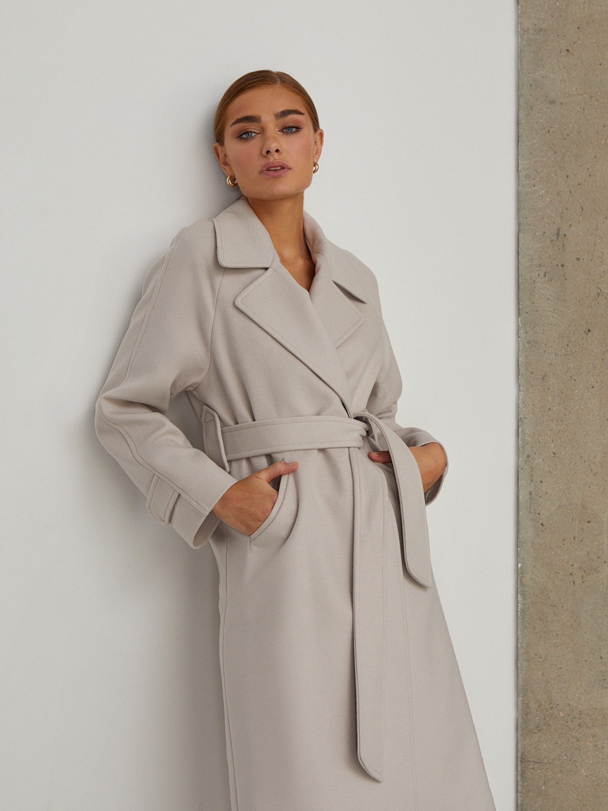 Пальто-халат длины миди с клапанами на карманах, рукавом реглан. Дополнено декоративными отстрочками и воротником-стойка с фигурным вырезом. Данная модель красиво подчеркивает женственные формы за счет пояса.

На модели размер XS