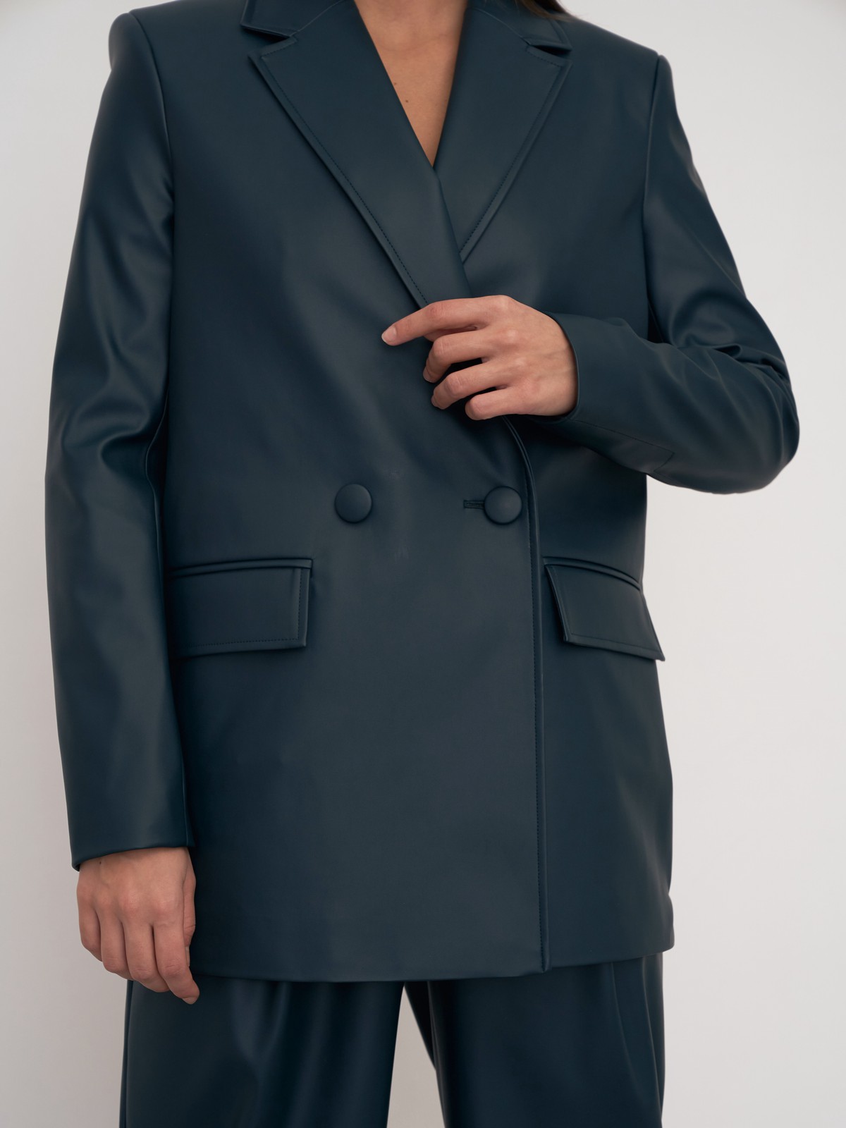 Жакет двубортного кроя выполнен из эко-кожи и оформлен заостренными лацканами, акцентированной плечевой линией и карманными клапанами по бокам.

На модели размер XS