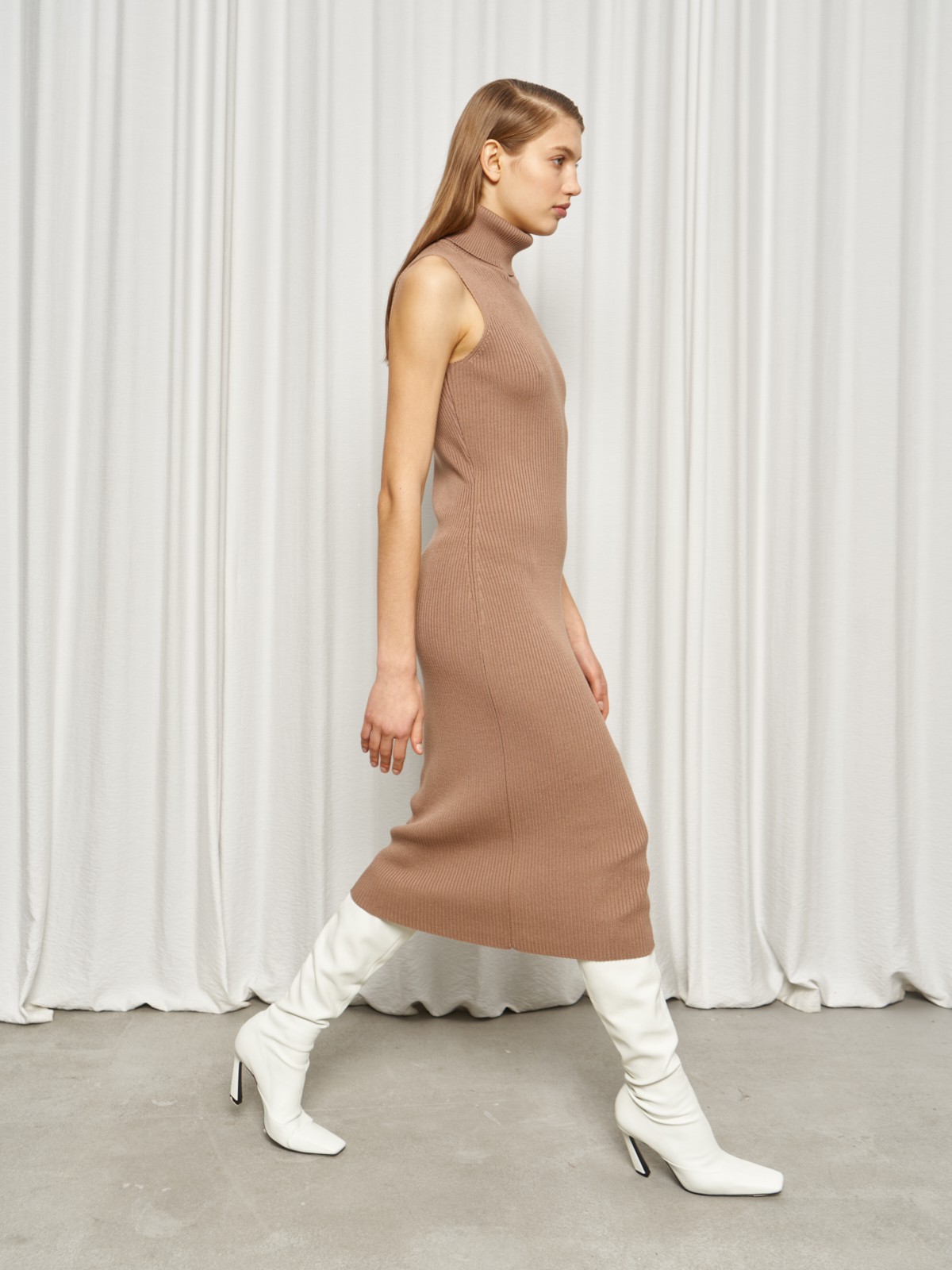 Платье без рукавов из вязаного трикотажа оформлено высокой горловиной-стойкой. Посадка по фигуре.

На модели размер XS