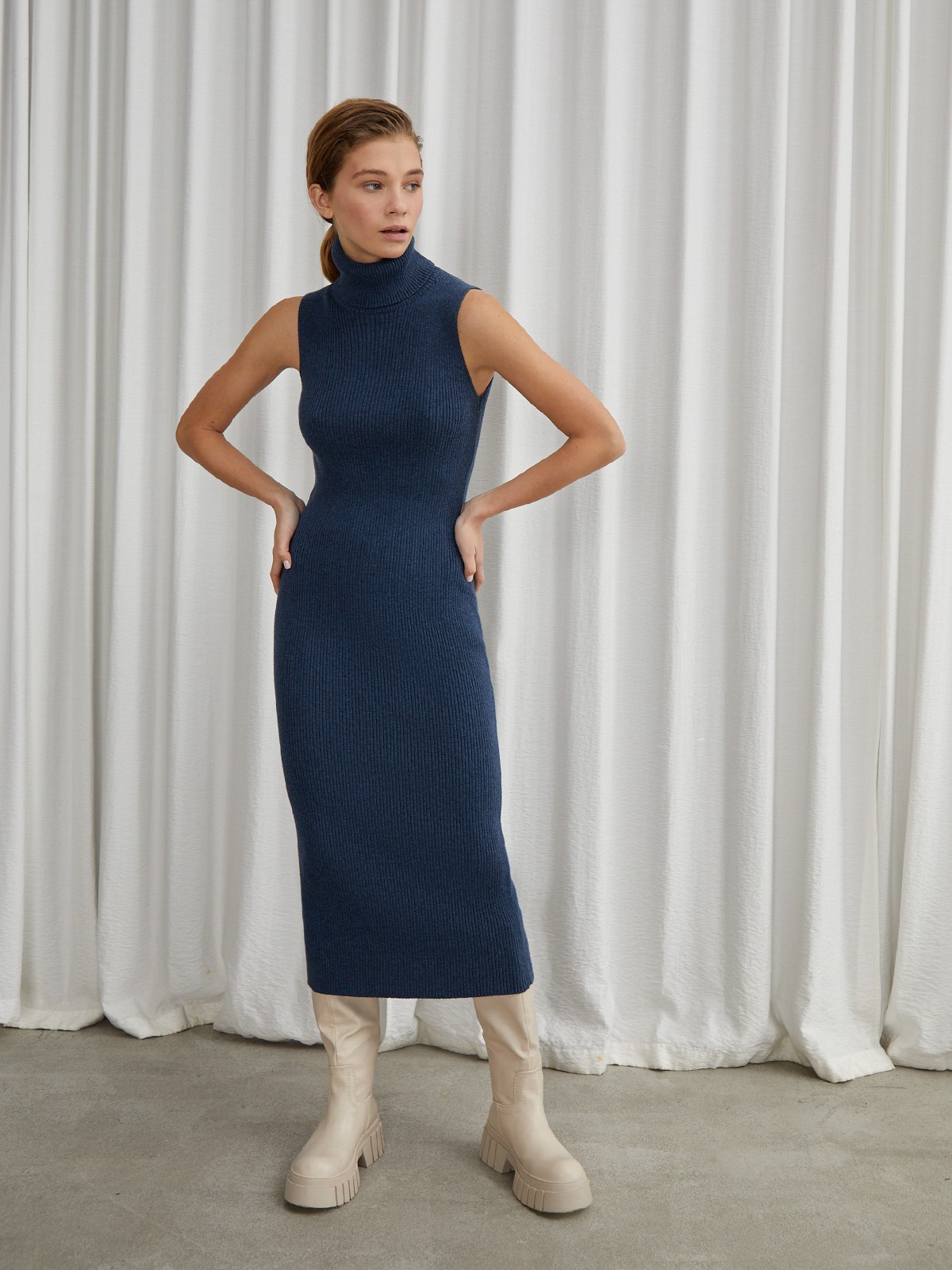 Платье без рукавов из вязаного трикотажа оформлено высокой горловиной-стойкой. Посадка по фигуре.

На модели размер XS