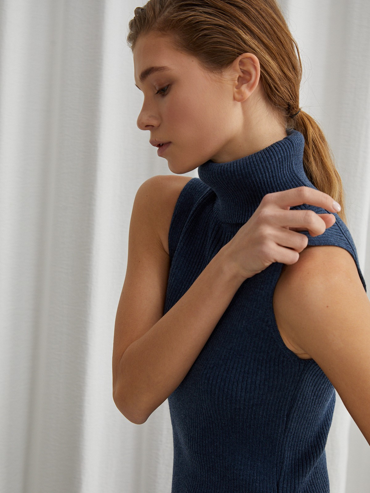 Платье без рукавов из вязаного трикотажа оформлено высокой горловиной-стойкой. Посадка по фигуре.

На модели размер XS