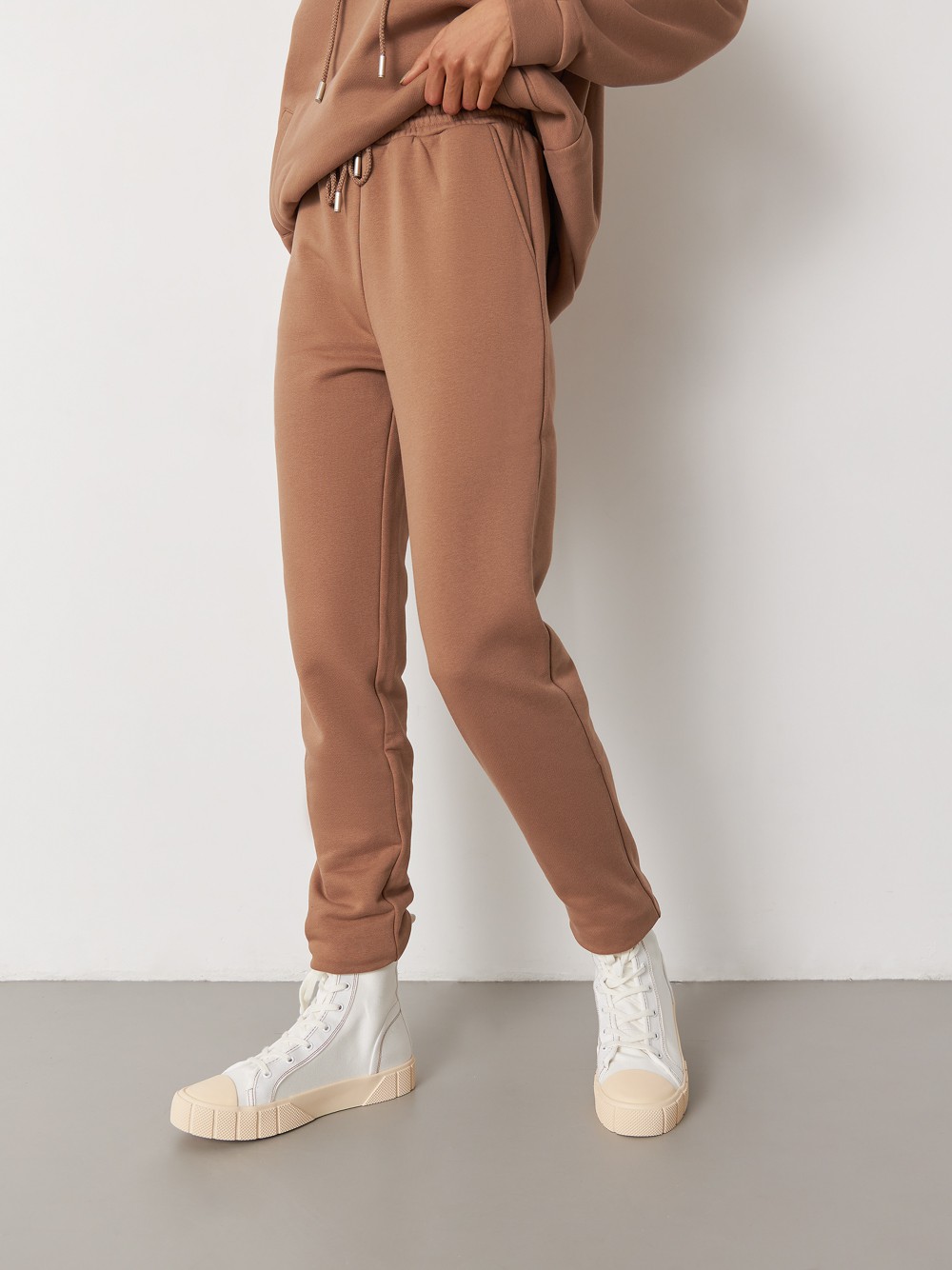 Брюки свободного спортивного силуэта. Модель дополнена манжетами из основной ткани по низу изделия и карманами по боковым швам. На поясе у брюк пояс, регулируемый завязками. Дополните свой образ толстовкой в тон изделия.

На модели размер XS