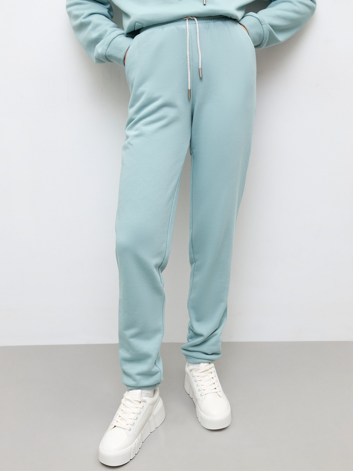 Брюки свободного спортивного силуэта. Модель дополнена манжетами из основной ткани по низу изделия и карманами по боковым швам. На поясе у брюк пояс, регулируемый завязками. Дополните свой образ толстовкой в тон изделия.

На модели размер XS