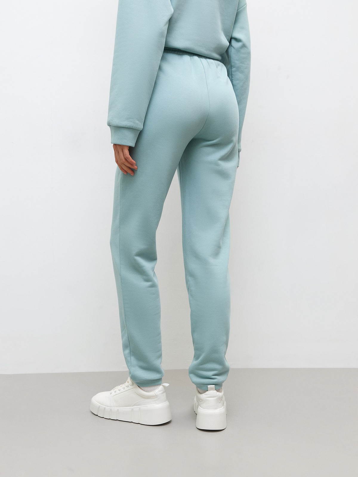 Брюки свободного спортивного силуэта. Модель дополнена манжетами из основной ткани по низу изделия и карманами по боковым швам. На поясе у брюк пояс, регулируемый завязками. Дополните свой образ толстовкой в тон изделия.

На модели размер XS