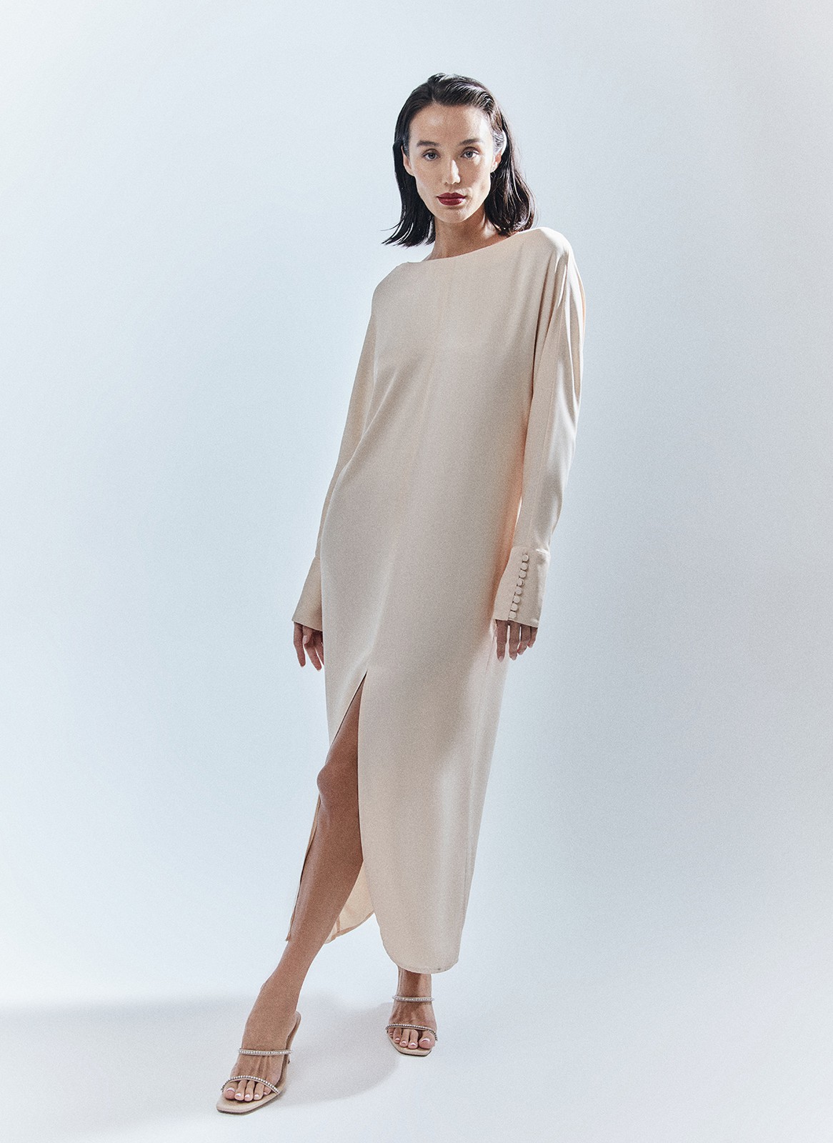 Платье длины миди с разрезом спереди. Свободный крой, деликатное сияние и струящийся материал. Акцентная деталь длинные манжеты с рядом декоративных пуговиц. На спине есть красивый V-образный вырез. Мы создали модель для праздничных моментов, но её легко добавить в гардероб на каждый день благодаря длинному рукаву и сдержанной зоне декольте. Носите для ощущения свободы в движениях или подчеркните талию широким поясом-кушаком ещё одним связующим звеном коллекции. Этот элемент костюма с восточными корнями в старину использовали и для хранения мелочей, и для утепления. Мы же оставили ему декоративное назначение.


