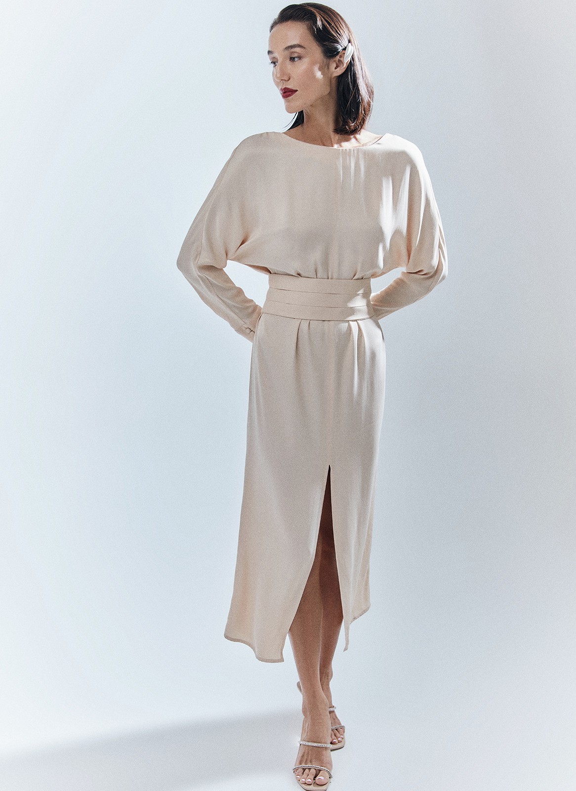 Платье длины миди с разрезом спереди. Свободный крой, деликатное сияние и струящийся материал. Акцентная деталь длинные манжеты с рядом декоративных пуговиц. На спине есть красивый V-образный вырез. Мы создали модель для праздничных моментов, но её легко добавить в гардероб на каждый день благодаря длинному рукаву и сдержанной зоне декольте. Носите для ощущения свободы в движениях или подчеркните талию широким поясом-кушаком ещё одним связующим звеном коллекции. Этот элемент костюма с восточными корнями в старину использовали и для хранения мелочей, и для утепления. Мы же оставили ему декоративное назначение.

