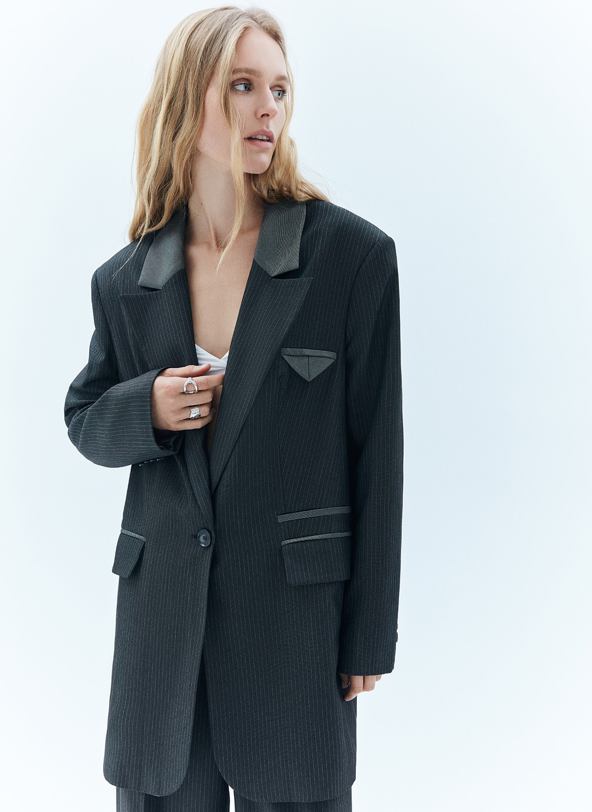 


Однобортный, удлинённый жакет свободного кроя. Благодаря фактуре материала имеет лёгкий деликатный блеск. Тонкая полоска тренд этой весны, идеально вписывающийся в морскую тему нашей коллекции и одновременно отсылающий нас к актуальному сейчас началу 2000-х. Лацканы выполнены из комбинации двух материалов (сияющего и более матового серого), предусмотрены двойные карманы с клапаном и контрастной отделкой, а также застёжка на одну пуговицу в тон. Имеет шлицу на спинке для комфорта, как и все наши жакеты.
Эффектный элемент модели маленький нагрудный кармашек с листочкой.
